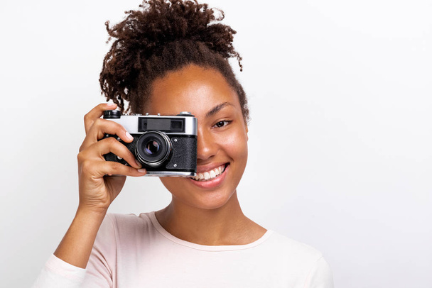Acercamiento Retrato de una feliz chica mulata viajera con cámara fotográfica en la mano y mirándola - Imagen
 - Foto, Imagen