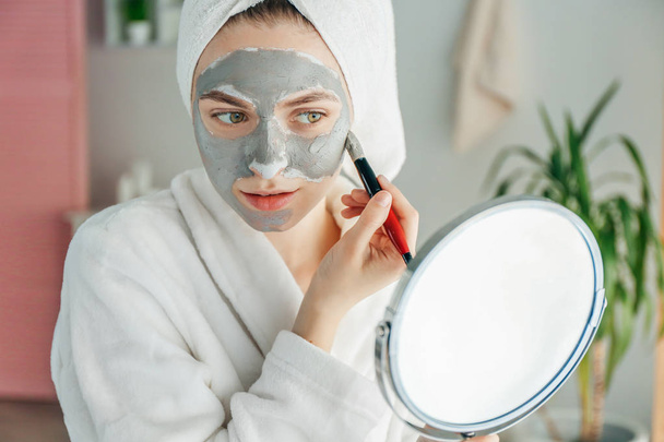 Mujer joven aplicando máscara de arcilla en casa
 - Foto, imagen