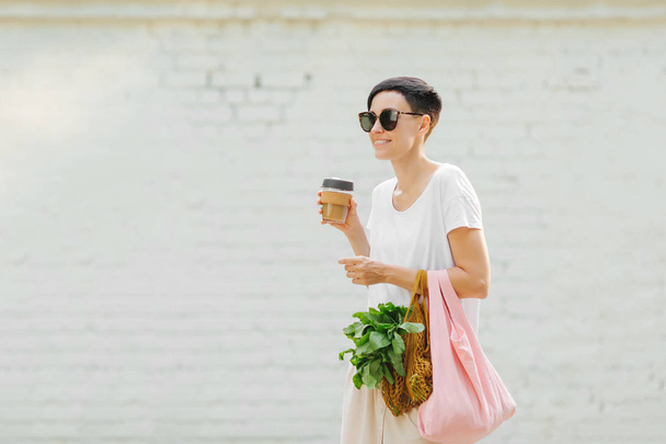 Young woman in light summer clothes with a eco bag of vegetables, greens and reusable coffee mug. Sustainable lifestyle. Eco friendly concept. - Fotoğraf, Görsel