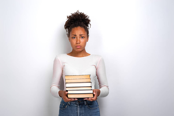 Sad unhappy young girl holding books standing in studio white background. Back to school - Valokuva, kuva