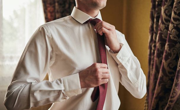 man in shirt dressing up and adjusting tie on neck at home - Photo, Image