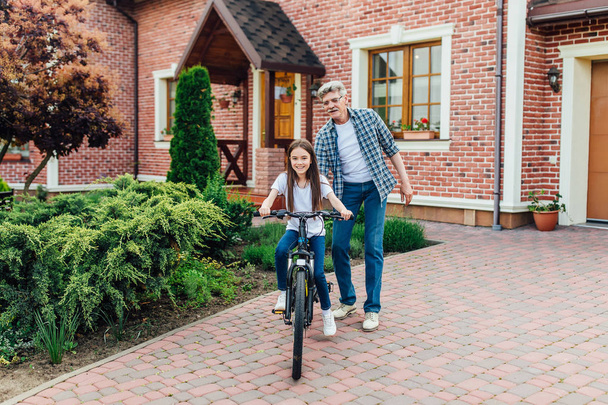 Handsome grandfather learning granddaughter to ride bike - Photo, Image