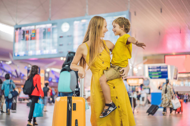 Family at airport before flight. Mother and son waiting to board at departure gate of modern international terminal. Traveling and flying with children. Mom with kid boarding airplane. yellow family - 写真・画像
