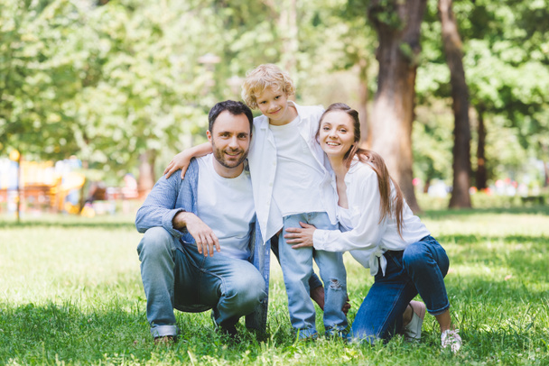 happy family looking at camera and hugging in park - 写真・画像
