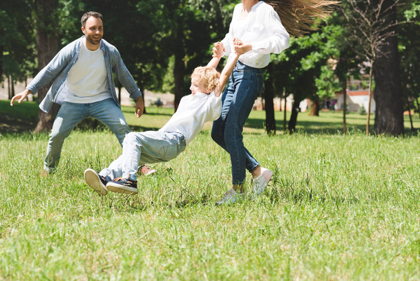 family spending time together, woman spinning son in park - Fotó, kép