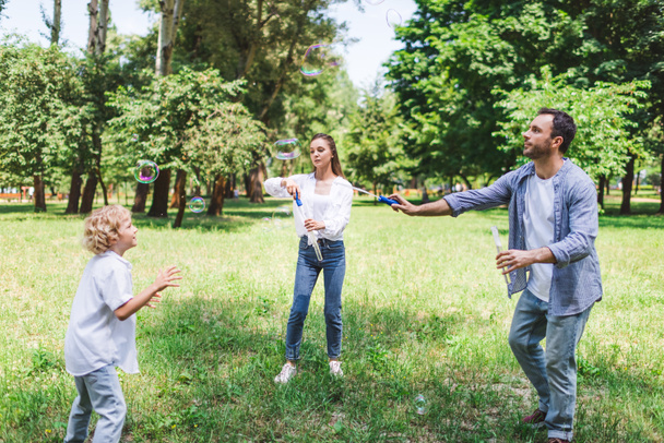 madre, padre e hijo jugando con burbujas de jabón en el parque durante el día
 - Foto, Imagen