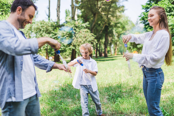 beautiful mother, father and son playing with soap bubbles in park - Photo, Image