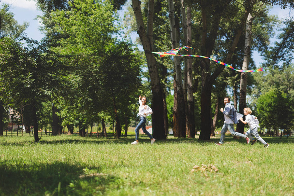 excited family running and playing with flying kite in park - Foto, Bild