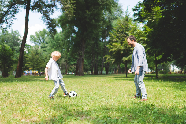 father and adorable son playing football in park together - Фото, изображение