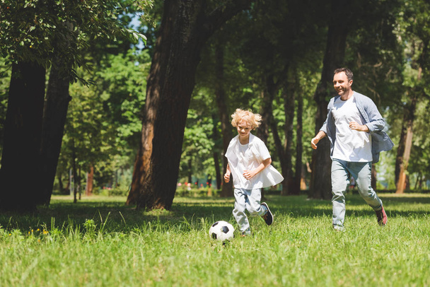 father and adorable son playing football with soccer ball in park with copy space - Φωτογραφία, εικόνα