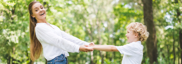 panoramic shot of beautiful smiling mom and son holding hands in park - 写真・画像