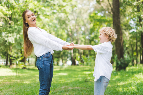 beautiful smiling mom and son holding hands in park - Photo, image