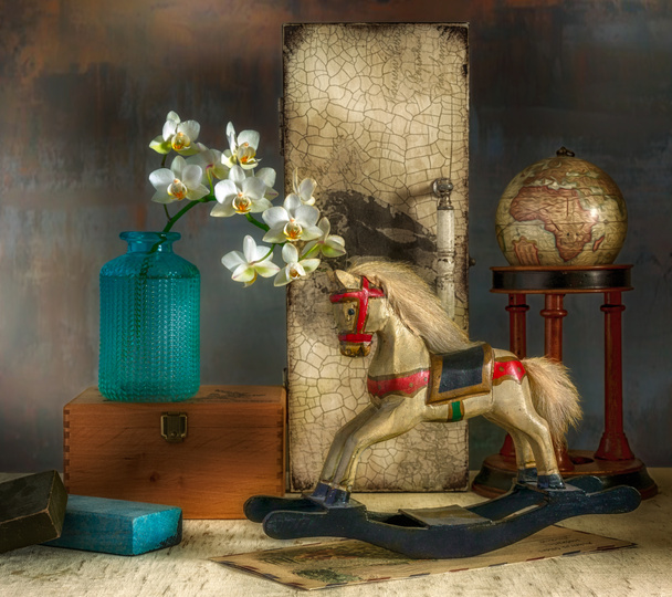Still life with a branch of a blossoming orchid, a wooden horse and a globe. Vintage. Retro. - Photo, Image