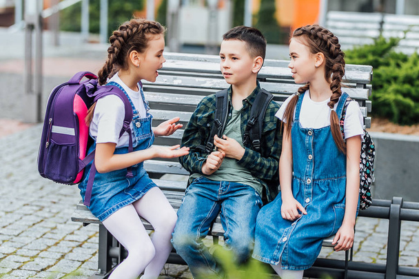 group of happy elementary school students with backpacks sitting near school - Fotografie, Obrázek