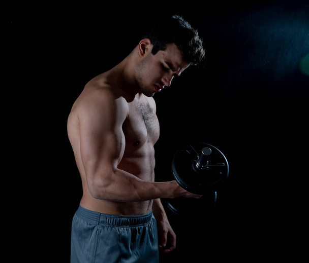 Portrait of young muscular built athlete man working out doing exercises and posing with dumbbells, bodybuilder male naked torso lifting weights in Fitness sports Body care and healthy lifestyle. - Photo, Image