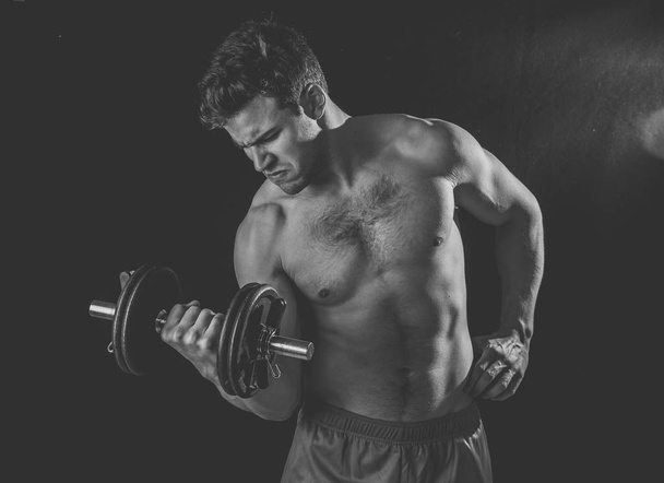 Portret van jonge gespierde atleet man uit te werken oefeningen en poseren met dumbbells, bodybuilder mannelijk naakte torso tillen gewichten in fitness sport lichaamsverzorging en gezonde levensstijl. - Foto, afbeelding
