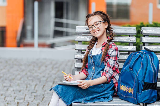 schoolgirl with backpack outdoors, reading book and doing homework - 写真・画像