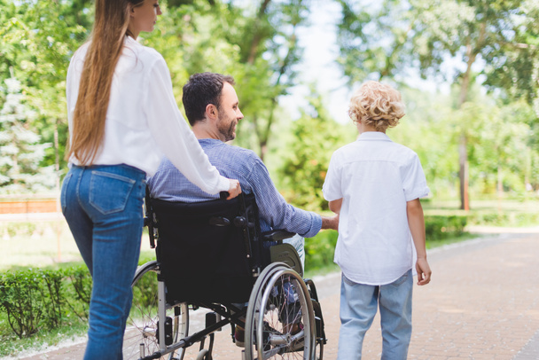 vista trasera de la madre silla de ruedas rodante con padre discapacitado en el parque
  - Foto, Imagen