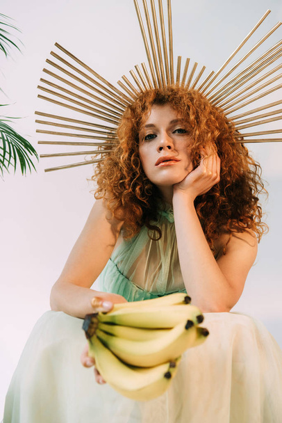 stylish redhead woman with accessory on head posing with bananas - Photo, Image
