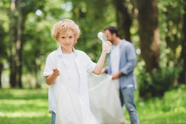 schattig jongen met plastic zak oppakken van vuilnis met vader in Park - Foto, afbeelding