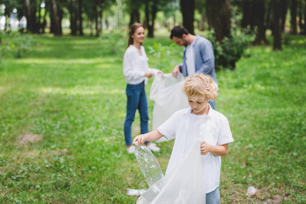 family picking up garbage in plastic bags in park with copy space - Foto, imagen