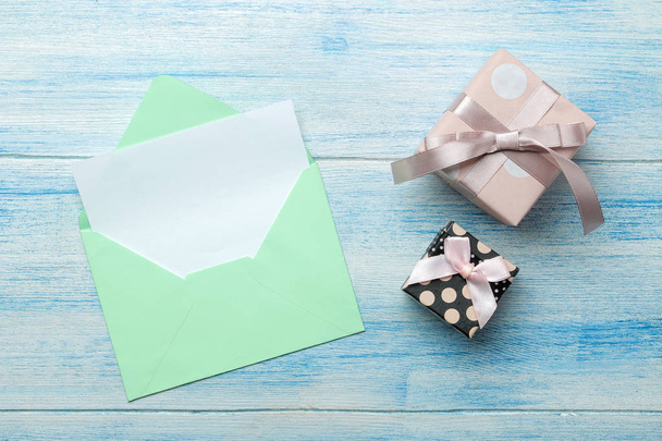a multi-colored envelope with an inscription letterhead and a gift box on a blue wooden table. top view - Photo, Image