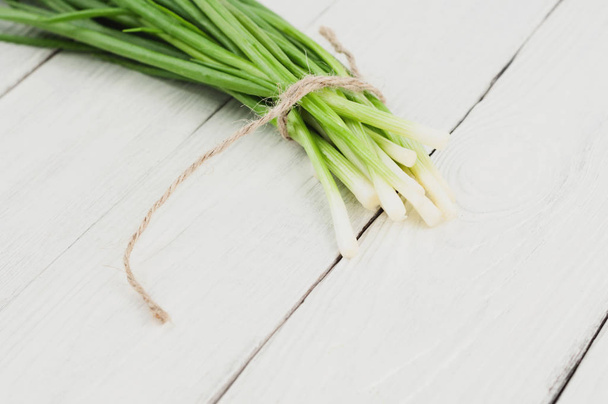 Tied green fresh onion on old white rustic wooden table - Foto, afbeelding