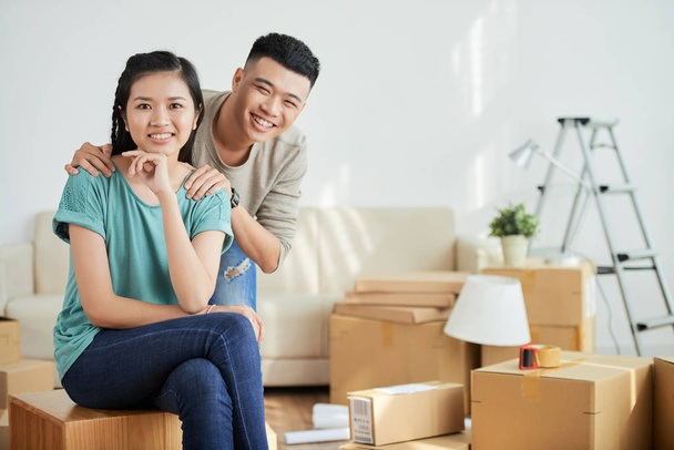 junge asiatische Männer und Frauen lächeln und blicken in die Kamera, während sie gemeinsam in eine neue Wohnung ziehen - Foto, Bild