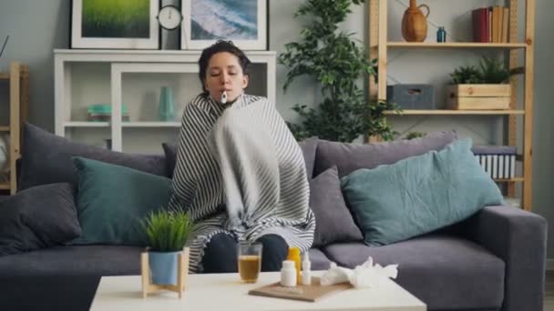 Jovencita enferma comprobando temperatura con termómetro en boca en apartamento
 - Metraje, vídeo