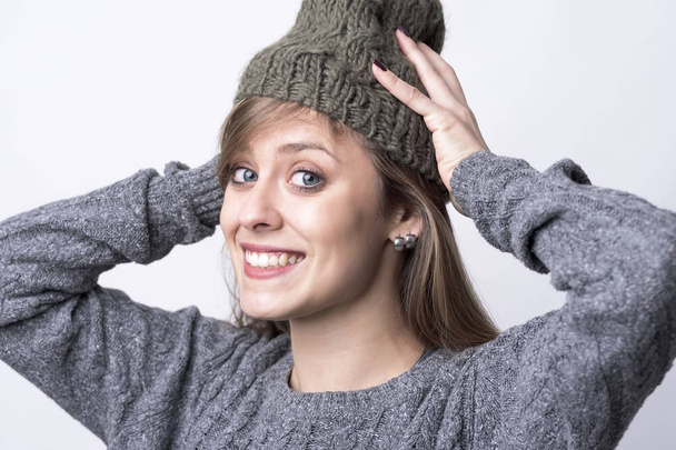 Милая очаровательная счастливая женщина надела шапочку, готовясь к холодной зимней погоде на светло-сером фоне
.  - Фото, изображение