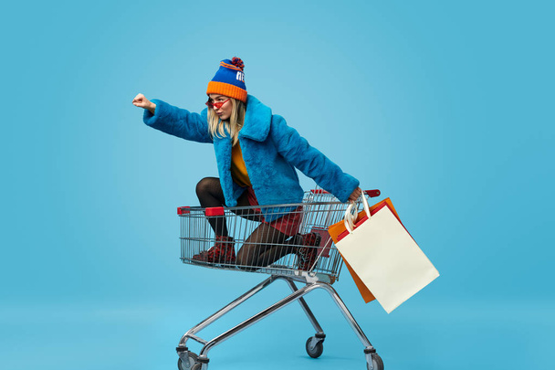 Young woman with shopping bags riding trolley - Foto, imagen