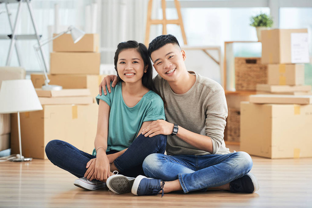 Iloinen nuori aasialainen pari istuu lattialla asunnossa
  - Valokuva, kuva