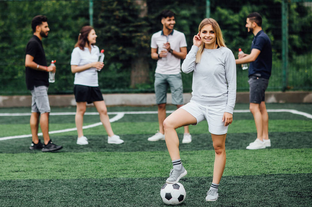 friends at field, young woman with soccer ball in foreground - Фото, зображення