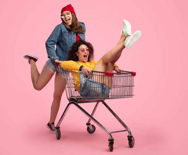 Cheerful young woman pushing shopping cart with friend - Foto, afbeelding