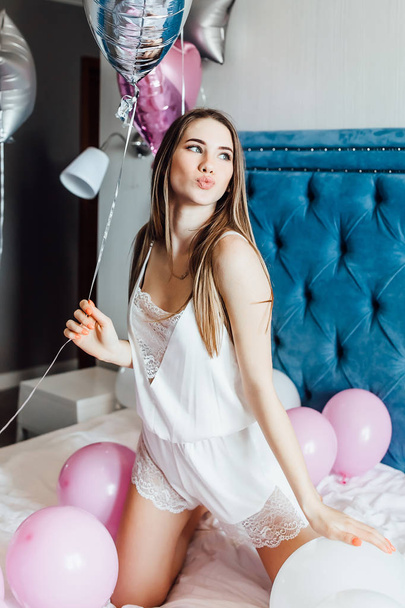 woman in sleepwear posing at camera on bed with balloons - Фото, изображение