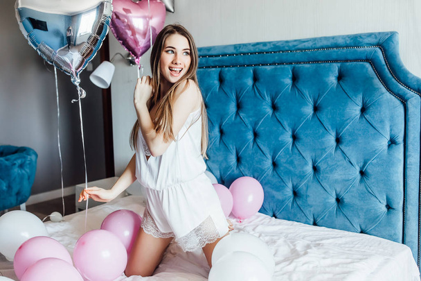vrouw in nachtkleding poseren op de camera op bed met ballonnen - Foto, afbeelding