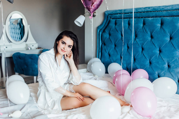 woman in sleepwear posing at camera on bed with balloons - Foto, afbeelding