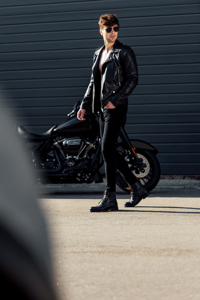 Selektiver Fokus eines jungen Mannes, der draußen neben schwarzem Motorrad steht - Foto, Bild