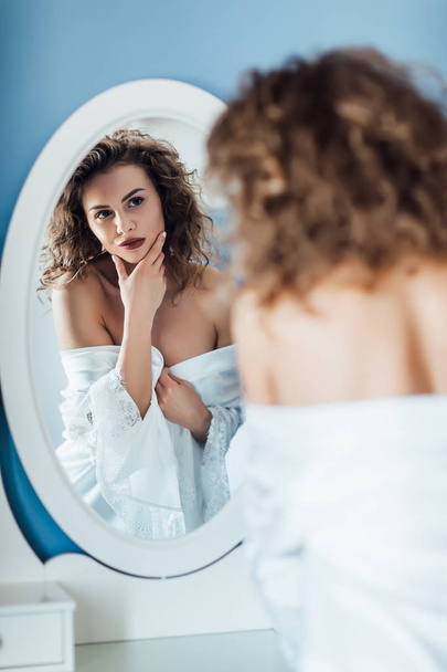 Young woman with curly hair looking in mirror - Valokuva, kuva