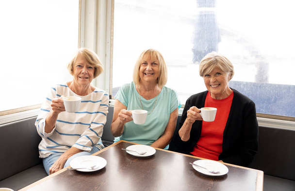 楽しい年配の友人が一緒にお茶やコーヒーを飲んでいます。退職後のライフスタイルや友情や交際の概念でアクティブな滞在でコーヒーショップで笑い、楽しんでおしゃべりするシニアガールフレンド. - 写真・画像
