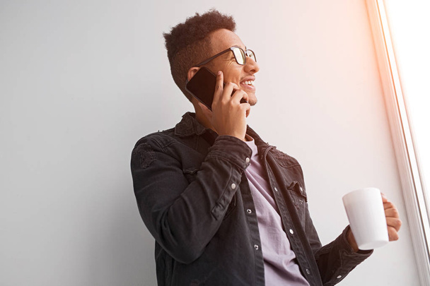 Smiling black man talking on phone and drinking coffee - Photo, Image