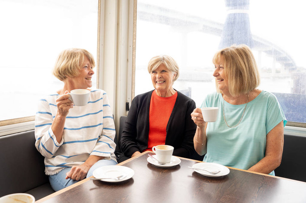 Joyful elderly friends having tea or coffee together. Senior girlfriends chatting laughing and having fun in coffee shop in Stay active in retirement lifestyle and friendship or companionship concept. - Photo, Image