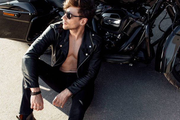 shirtless young man sitting on ground near black motorcycle - 写真・画像