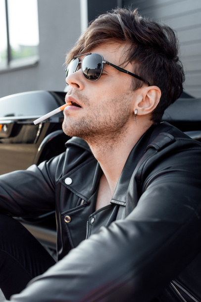 csinos fiatalember, a cigaretta és napszemüveg közelében ülve motorkerékpár - Fotó, kép