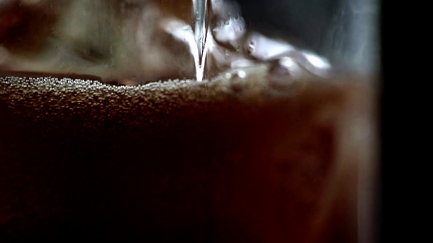 selective focus of cola flavored soda pouring in glass with frozen ice cubes isolated on black  - 映像、動画