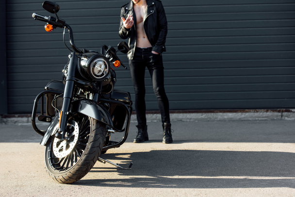 cropped view of motorcyclist smoking and standing near black motorcycle - Foto, Imagem