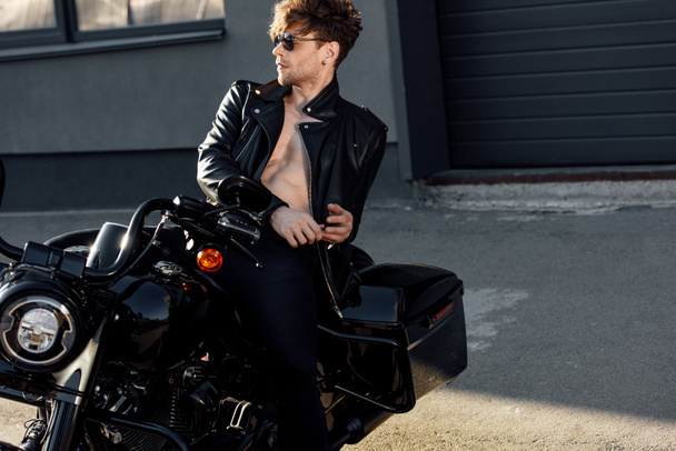 без рубашки молодой человек в кожаной куртке отдыхает на черном мотоцикле
 - Фото, изображение
