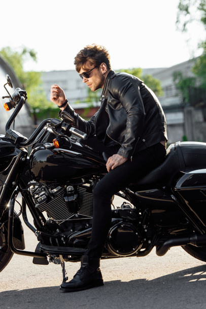 вид сбоку мотоциклиста в солнечных очках и кожаной куртке, сидящего на мотоцикле
 - Фото, изображение