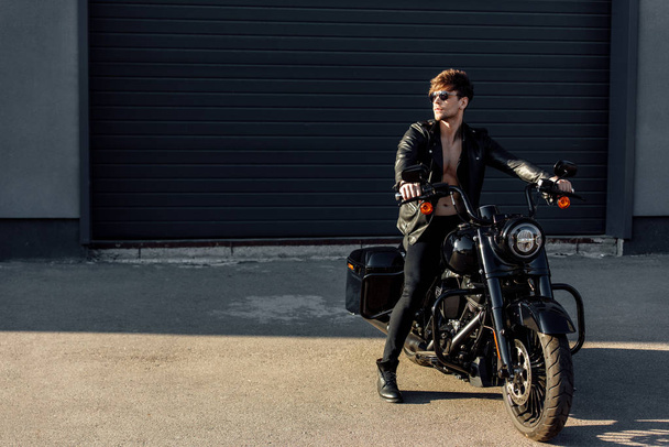 πλήρες μήκος του όμορφου άνδρα με γυμνό κορμό κάθεται σε μοτοσικλέτα και κοιτάζοντας μακριά - Φωτογραφία, εικόνα