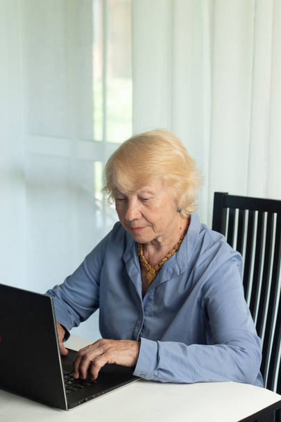 Starší šedovlasá žena s laptopem. Starší žena píše paměti v přenosném počítači, vyhledává informace na internetu nebo komunikuje online - Fotografie, Obrázek